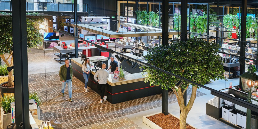 Een moderne, ruim opgezette winkel met verschillende displays, planten en klanten die rondlopen.