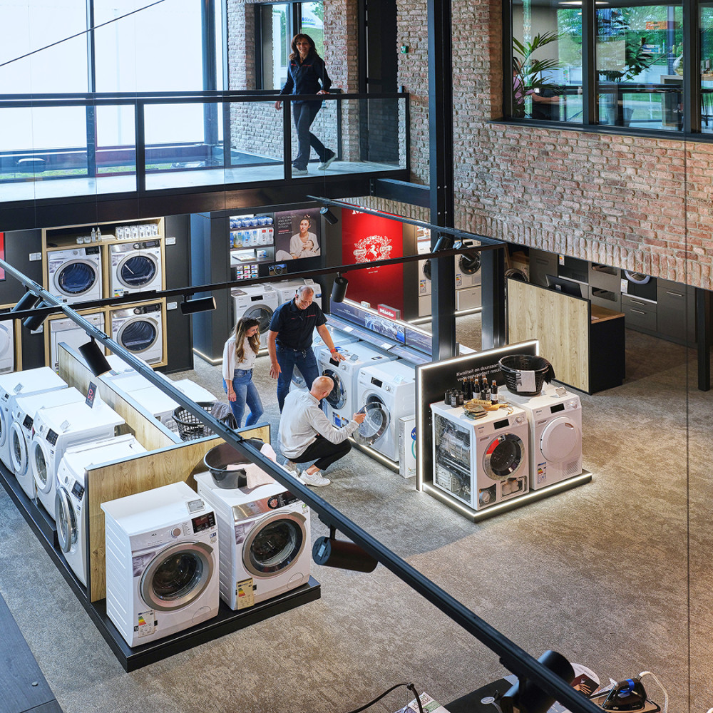 Een elektronicawinkel met wasmachines en mensen die apparaten bekijken.