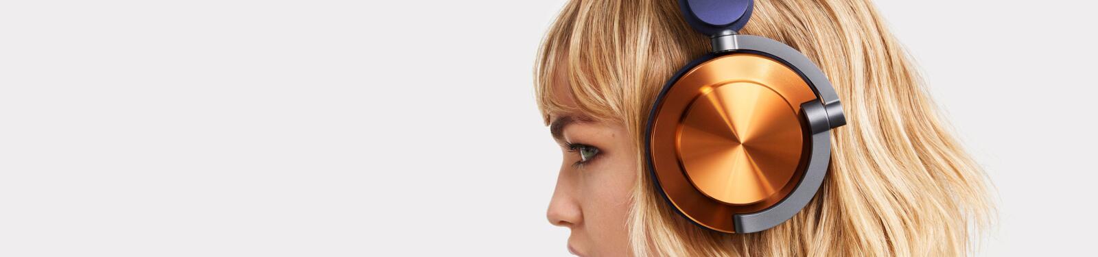 Een persoon met blond haar draagt een koptelefoon met oranje oorschelpen.