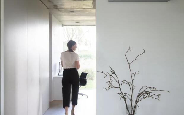 Een vrouw loopt door een moderne kamer met airco aan de muur en decoratieve takken op tafel.