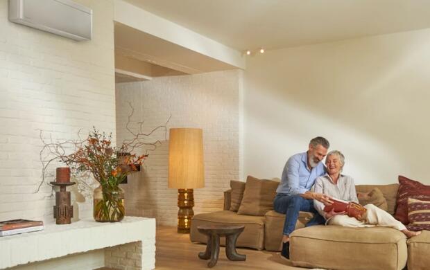 Een ouder koppel zit samen op een beige bank in een sfeervol ingerichte woonkamer.