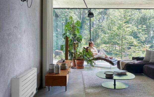 Moderne kamer met grote ramen, veel planten en een persoon die ontspant in een lounge stoel.