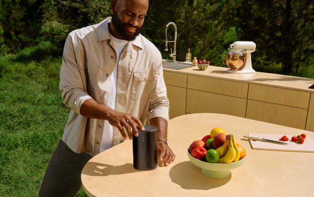 Man staat buiten bij tafel met speaker en schaal fruit.