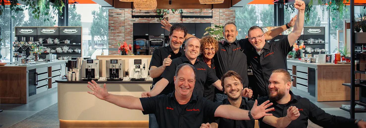 Een groep lachende mensen in een keukenwinkel, met blije gezichten en omarmende gebaren.