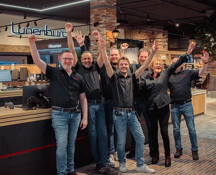Een groep mensen in zwarte shirts juicht enthousiast in een winkelomgeving.