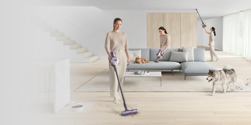 Vrouw stofzuigt een moderne woonkamer met open trap, een kat slaapt op de bank, een hond loopt rond en er zijn meerdere vrouwen die hetzelfde doen.