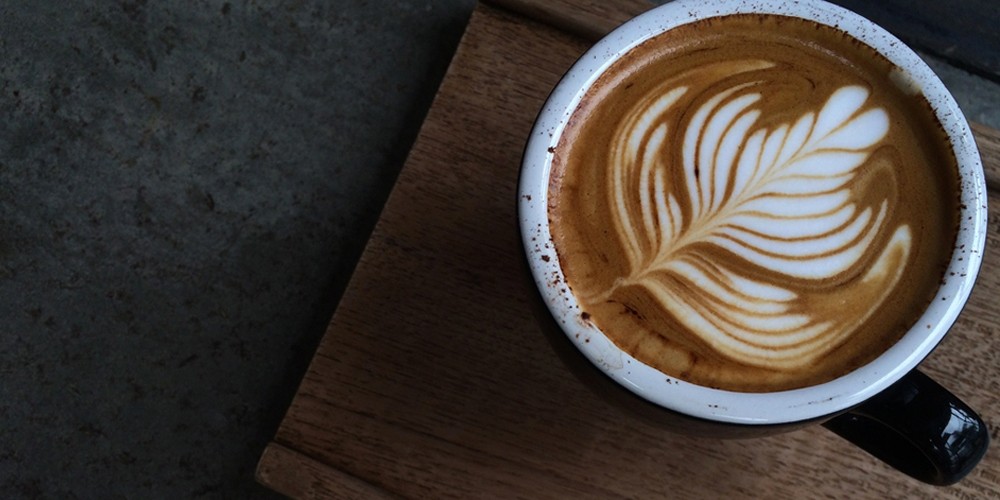 Een kop koffie met latte art in de vorm van een blad op een houten dienblad.