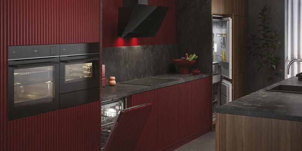 Moderne keuken met rode en zwarte elementen, oven, vaatwasser en open koelkast.