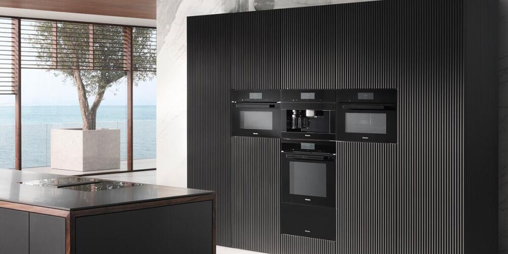 Moderne keuken met ingebouwde zwarte apparaten en groot raam met uitzicht op zee.