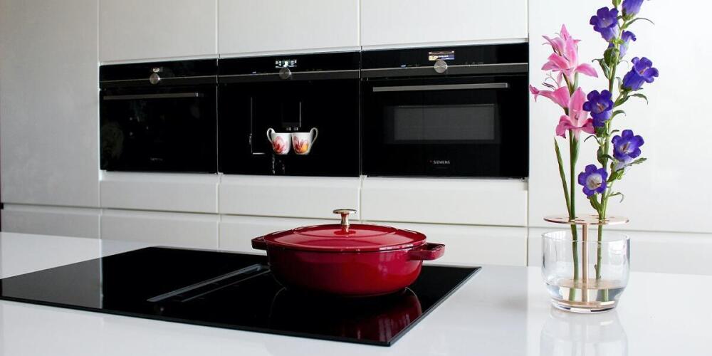 Rode pan op inductiekookplaat, bloemen in vaas, moderne keuken met ovens.