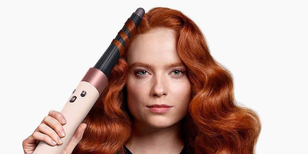 Vrouw met rood haar gebruikt een krultang om haar haar te stylen.