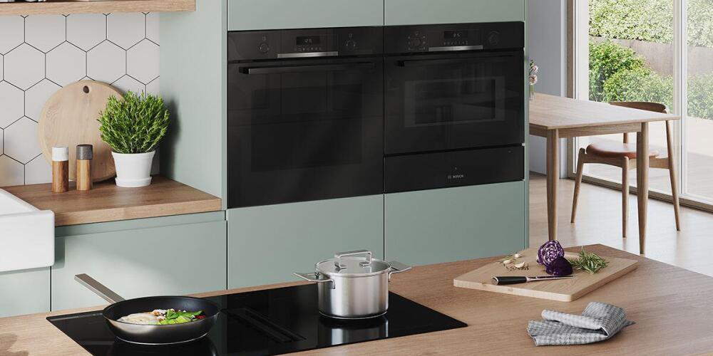 Moderne keuken met oven, kookplaat, snijplank en planten, met uitzicht op tuin.