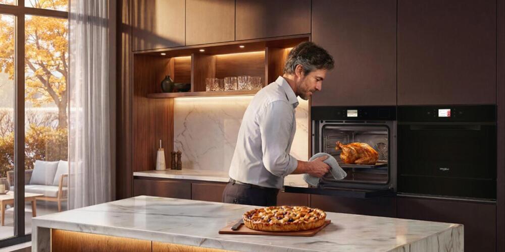 Man haalt een kalkoen uit de oven in een moderne keuken met marmeren aanrecht en herfstzicht.