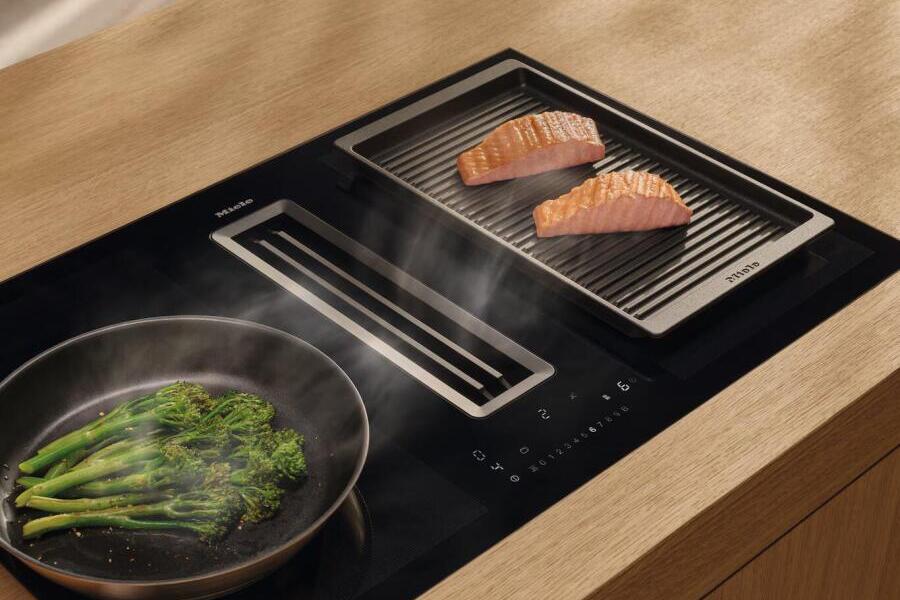 Kookplaat met grill, twee stukken zalm en broccoli in een pan.