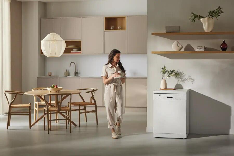 Een moderne keuken met een vrouw die een kopje vasthoudt, tafel en stoelen, en een vaatwasser.