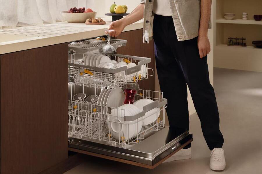 Iemand doet een open vaatwasser met borden en glazen in een keuken.