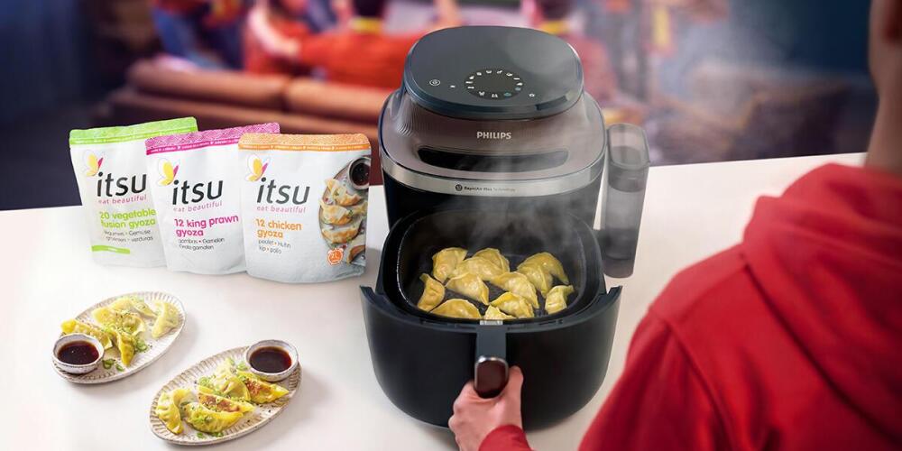 Iemand gebruikt een Airfryer om gyoza te bereiden, met Itsu gyoza-verpakkingen op de achtergrond.