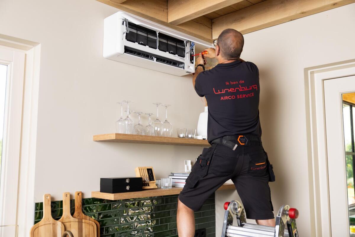 Een monteur op een ladder repareert een airconditioning aan de muur.