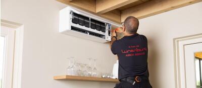 Een monteur op een ladder repareert een airconditioning aan de muur.