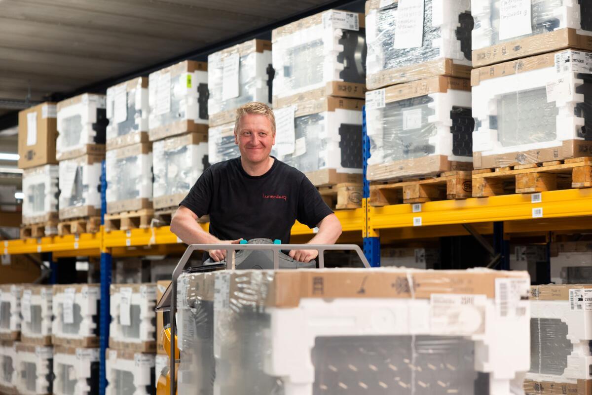 Man bestuurt een heftruck in een opslagruimte met gestapelde dozen op pallets.