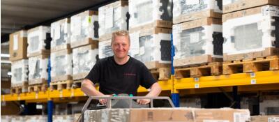 Man bestuurt een heftruck in een opslagruimte met gestapelde dozen op pallets.