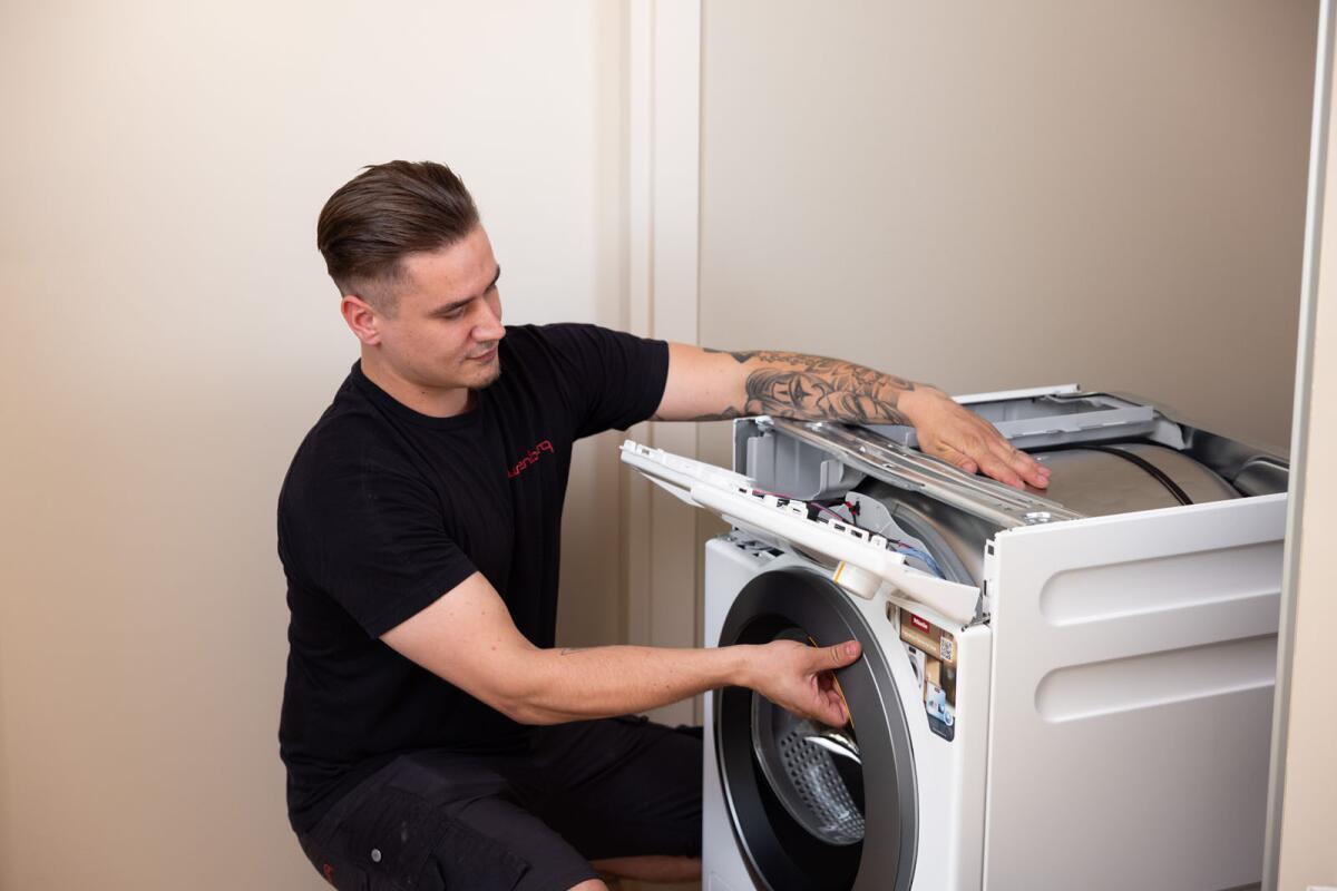 Een man repareert een wasmachine door de trommel en het paneel te controleren.