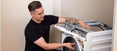 Een man repareert een wasmachine door de trommel en het paneel te controleren.
