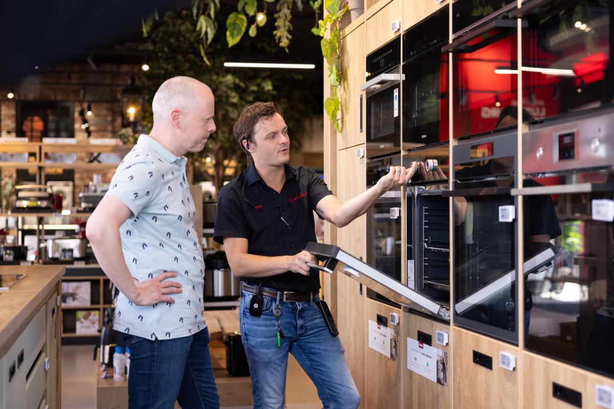 Twee mannen bespreken en bekijken een keukenapparaat in een winkelomgeving.